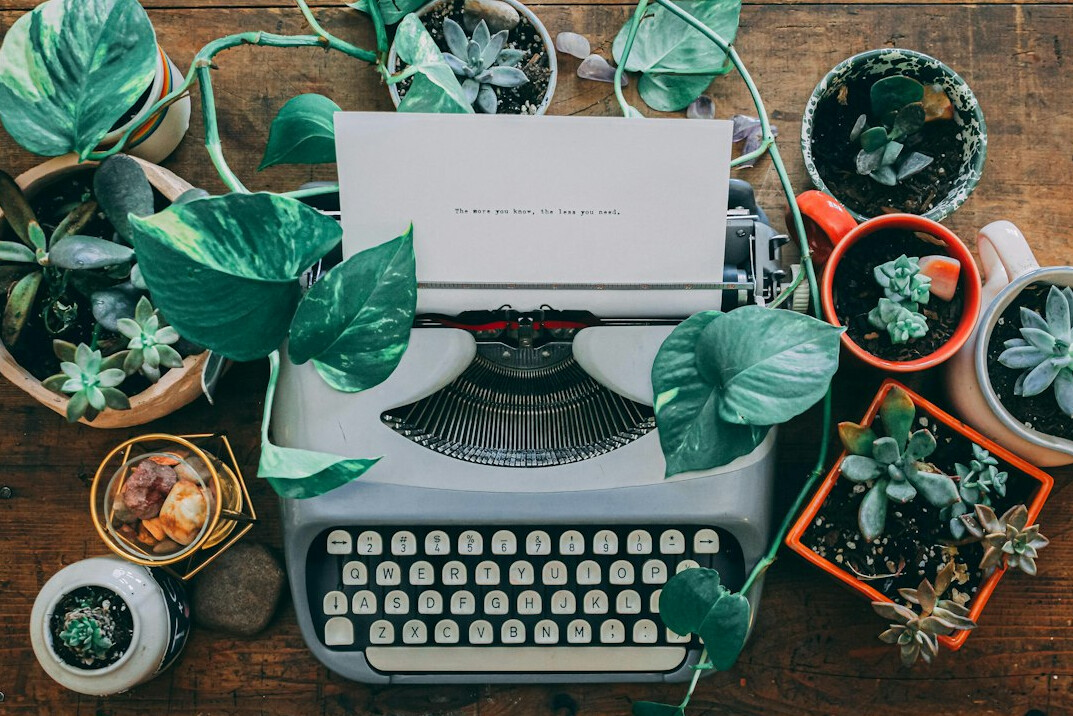 Overhead flat lay of a wooden writing desk with a typewriter, notebook and coffee cup